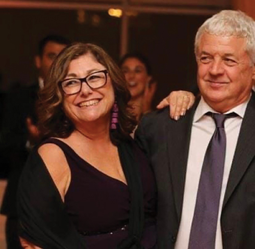 Kristine and Bill David, longtime community volunteers and supporters of Bradley Hospital dressed in formal attire smile warmly with one resting a hand on the other's shoulder in a dimly lit party setting.