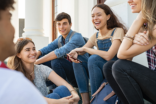A group of five people sitting on steps outdoors, smiling and engaging in conversation, with one person holding a smartphone.