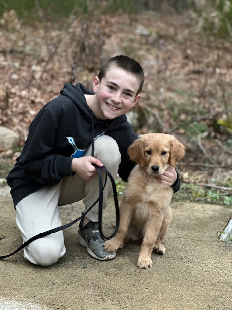 Young boy kneels next to golden retriever puppy