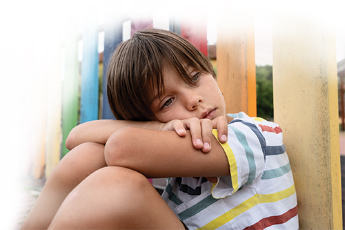 sad boy sitting on ground with head on arms