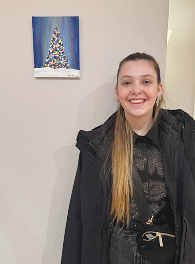 young patient stands next to artwork that she created hanging on a wall