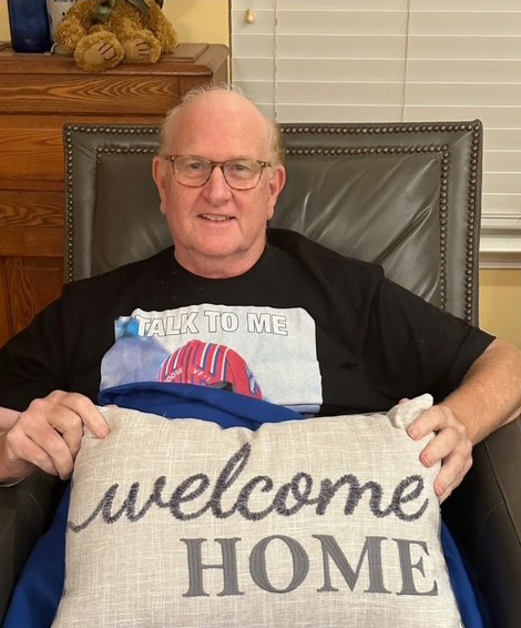 Older man sitting in a chair holding a Welcome Home pillow