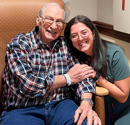 Biz sits in chair as caregiver sits by his side